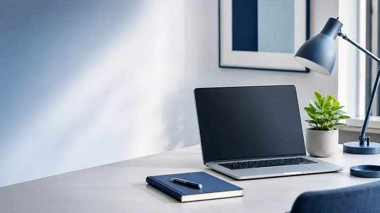 A clean desk with a laptop, notebook, lamp, and small plant in a bright workspace.